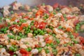Process of cooking paella with meat pieces, peppers, peas in huge wok - close up