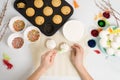 The process of decorating mini cupcakes Easter cakes with white icing and sweet candies, top view, willow branches and eggs for