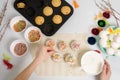 The process of decorating mini cupcakes Easter cakes with white icing and sweet candies, top view, willow branches and eggs for