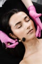 Process of face massage with black stone roller close-up. Cosmetologist using stone roller for face massage for girl