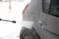 A process of flushing soap sud on silver car with pressurised water stream at self-service indoor car wash station