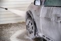 A process of flushing soap sud on silver car wheel with pressurised water stream at self-service indoor car wash station