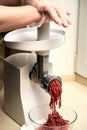 The process of grinding meat into minced meat in a meat grinder. Gloved hands push the meat into the meat grinder.