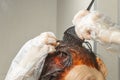 Process of hair dyeing in red colour using a brush. Young woman apply a red colour to her hair