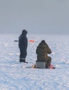 Process of ice fishing, group of fishermen on ice near tent shelter, with equipment in a winter snowy day, tents and ice auger on