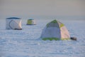 Process of ice fishing, group of fishermen on ice near tent shelter, with equipment in a winter snowy day, tents and ice auger on Royalty Free Stock Photo