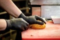 The process of making a burger in a restaurant kitchen. The chef in black gloves cut the bun.