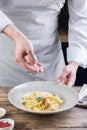 Process of making a pasta dish. Chef sprinkles Italian pasta with grated cheese.