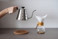 Process of making pour over coffee. Woman hand holding kettle over hand drip coffee maker