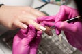 process of performing manicure in beauty salon. manicurist in pink gloves painting nails on hands of client with white shellac.