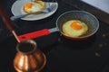 Process of preparing a classic breakfast: fried eggs in a frying pan, a classic Turkish Turk for cooking coffee on a glass hob.