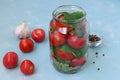 The process of preparing pickled tomatoes with grape leaves and garlic. Location on a light blue background