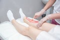 The process of sugar depilation. Master in medical gloves puts a red paste on the client`s leg
