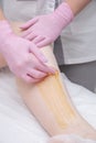 The process of sugar depilation. Master in medical gloves puts a yellow paste on the client`s leg