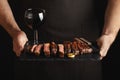 Man holding juicy grilled beef steak with spices and red wine glass on a stone cutting board on a black background Royalty Free Stock Photo