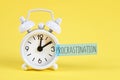 Procrastination, delay, urgency concept. White alarm clock with text procrastination