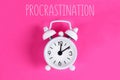 Procrastination, delay, urgency concept. White alarm clock with text procrastination