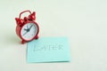 Procrastination, postpone or laziness concept, red alarm clock on sticky note with handwriting the word Later on office table