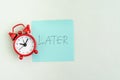 Procrastination, postpone or laziness concept, red alarm clock on sticky note with handwriting the word Later on office table