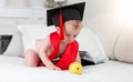 Prodigy baby in graduation cap and ribbon reaching for apple