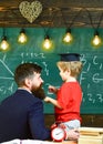 Prodigy child concept. Teacher with beard, father teaches little son in classroom, chalkboard on background. Boy, child