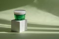 Product concept for beauty and body care on white 3D podium. Green jar of cream on white square stand. Shadows from