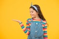 Product presentation. Kid happy smiling face show something on open palm copy space yellow background. Girl demonstrate