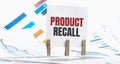 PRODUCT RECALL text on paper sheet with chart, dice, spectacles, pen, laptop and blue and yellow push pin on wooden table -