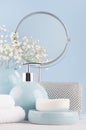 Products for body and skin care in light blue ceramic bowls, silver cosmetic bag, circle mirror and white flowers on wood table. Royalty Free Stock Photo