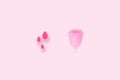 Products of the female intimate hygiene period. Top view of blood drops and pink silicone menstrual cup on a color background