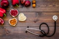 Products good for heart and blood vessels. Vegetables, fruits, nuts in heart shaped bowl near stethoscope on dark wooden Royalty Free Stock Photo