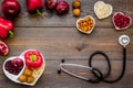 Products good for heart and blood vessels. Vegetables, fruits, nuts in heart shaped bowl near stethoscope on dark wooden Royalty Free Stock Photo
