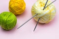 Products for needlework, knitting. Balls of yellow, green, purple yarn, knitting needles on a pink background.