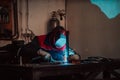 Profesional welder in protective uniform and mask welding metal pipe on the industrial table with other workers behind