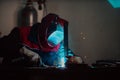 Profesional welder in protective uniform and mask welding metal pipe on the industrial table with other workers behind