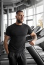 Professioal Occupation. Bearded trainer standing at gym leaning on treadmill pensive