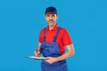 Profession, construction and building - handsome male worker or builder in blue cap with clipboard. Blue studio bakcground. Royalty Free Stock Photo