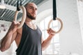 Muscular man holding gymnastic rings at light gym and looking away Royalty Free Stock Photo