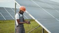 Professional african engineer in helmet and uniform using multimeter for measuring amperage in solar panels. Concept of