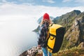 Professional alone expeditor wearing backpack and red hat standing on the edge cliff mountain. Extreme tourist on high rock above