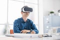 Professional architect working at office desk and wearing a VR headset, he is viewing a virtual reality interface