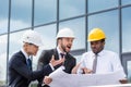 Professional architects in hardhats discussing blueprint outside modern building Royalty Free Stock Photo