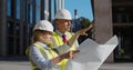 Professional architects in helmet studying blueprint outside modern building. Royalty Free Stock Photo