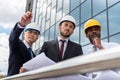 Professional architects in helmets working with blueprint outside modern building Royalty Free Stock Photo