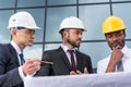 Professional architects in helmets working with blueprint outside modern building Royalty Free Stock Photo