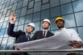 Professional architects in helmets working with blueprint outside modern building Royalty Free Stock Photo