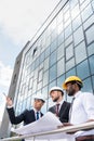 Professional architects in helmets working with blueprint outside modern building