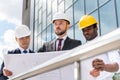 Professional architects in helmets working with blueprint outside modern building Royalty Free Stock Photo