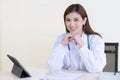 Professional Asian beautiful young smiling female doctor sitting in office at hospital. On table has a clipboard and digital Royalty Free Stock Photo