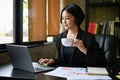 Professional Asian businesswoman focuses on her work on laptop and sipping coffee Royalty Free Stock Photo